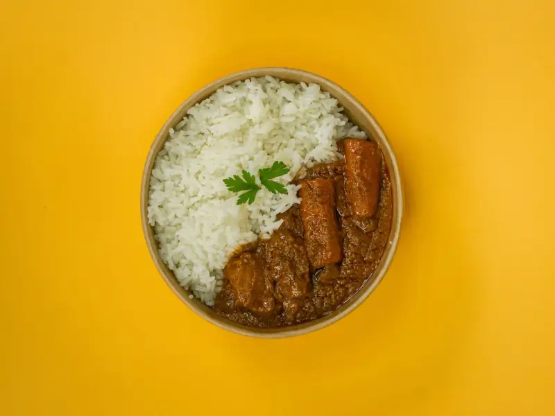 Overhead bowl of steamed white rice with a rich brown stew and a parsley garnish
