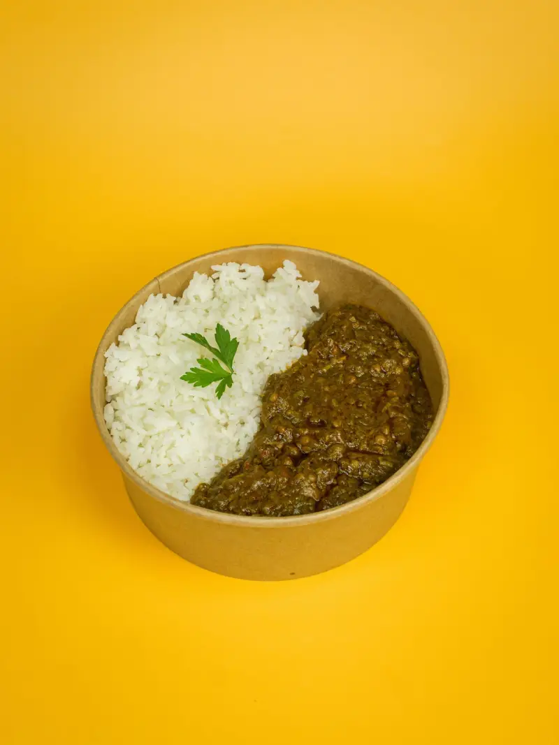 Bowl of white rice served with a dark, slow-cooked leafy stew, shot from a low angle