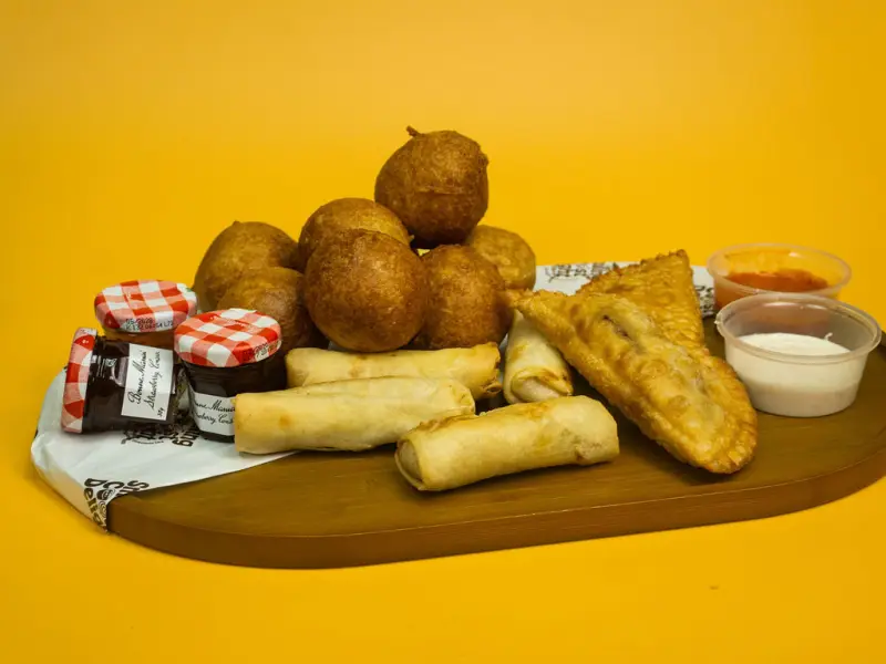Wooden board of fried dough balls, spring rolls and pastries with jam and dipping pots